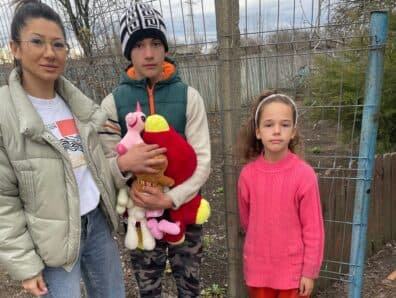 O mamă și doi copii cu jucăriile de pluș primite, la poarta curții
